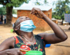 农村的一名妇女把一片药片放在嘴里，头向后仰着。她的另一只手拿着一杯水。