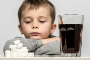 一个小孩把下巴搁在胳膊上，看着桌上的一堆方糖和一杯碳酸可乐