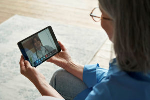 戴着眼镜的病人手持一个电子平板电脑，上面有与护士的视频通话