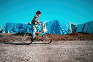 一个孩子骑着自行车经过难民营的帐篷